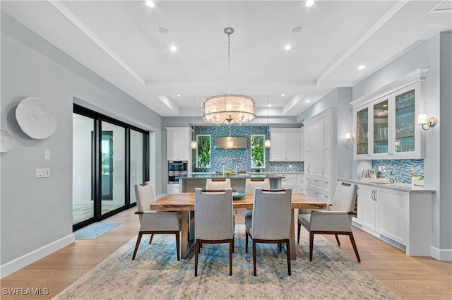 dining space with a raised ceiling, sink, an inviting chandelier, and light hardwood / wood-style floors