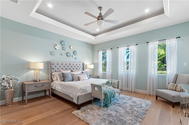 bedroom featuring a raised ceiling, ceiling fan, and light hardwood / wood-style flooring