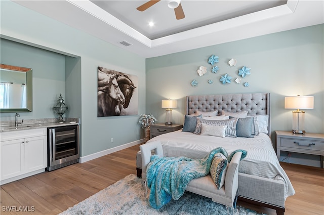 bedroom with ceiling fan, beverage cooler, a raised ceiling, and sink