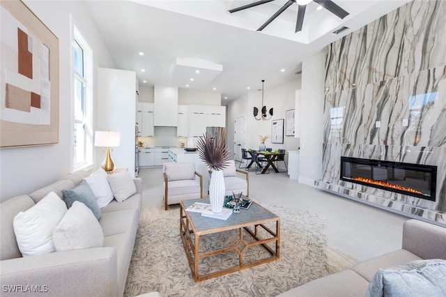 living room with ceiling fan, a fireplace, light carpet, and a high ceiling