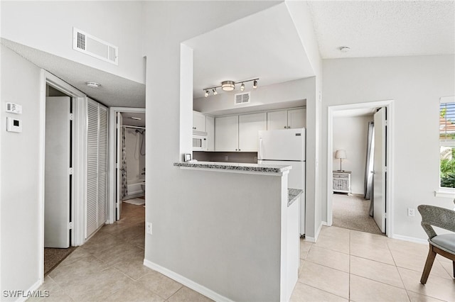 kitchen with white cabinetry, kitchen peninsula, a textured ceiling, and light tile patterned floors