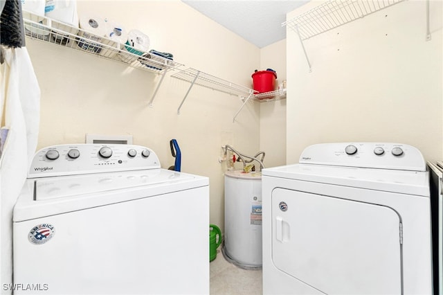 clothes washing area with electric water heater, a textured ceiling, and washer and clothes dryer