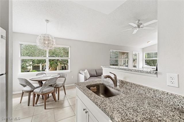 kitchen with sink, vaulted ceiling, decorative light fixtures, light tile patterned floors, and white cabinets