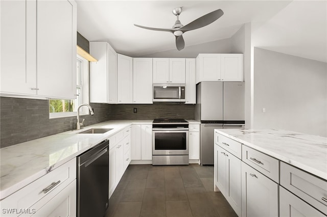 kitchen with stainless steel appliances, vaulted ceiling, white cabinets, sink, and light stone countertops