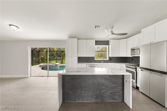 kitchen with light stone counters, stainless steel appliances, a kitchen island, white cabinetry, and sink