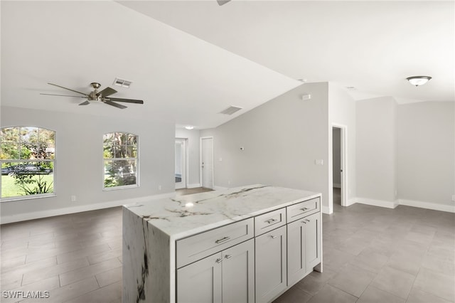 kitchen with ceiling fan, a center island, vaulted ceiling, and light stone countertops