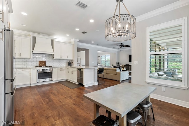 kitchen featuring appliances with stainless steel finishes, kitchen peninsula, decorative light fixtures, white cabinets, and premium range hood