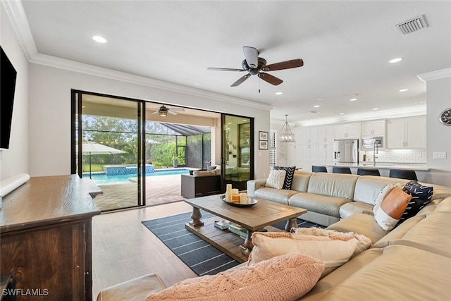 living room with ornamental molding, wood-type flooring, and ceiling fan with notable chandelier