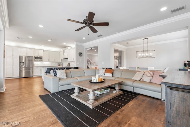 living room with crown molding, sink, ceiling fan with notable chandelier, and light wood-type flooring