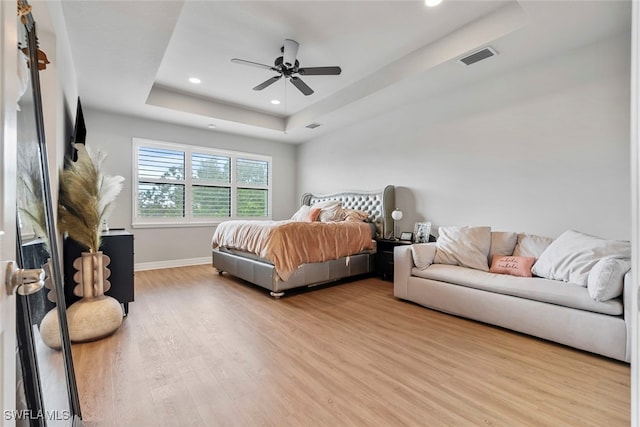 bedroom with ceiling fan, a raised ceiling, and light hardwood / wood-style flooring