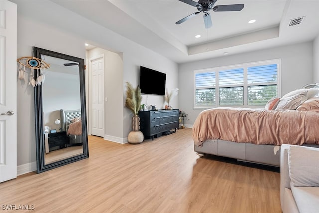 bedroom with ceiling fan, a raised ceiling, and light wood-type flooring