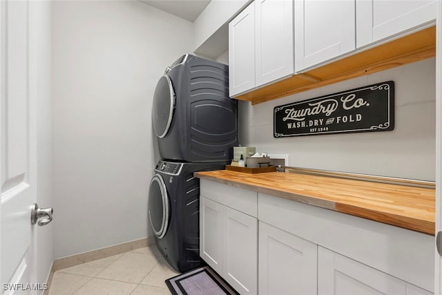 clothes washing area featuring stacked washer / drying machine, cabinets, and light tile patterned floors