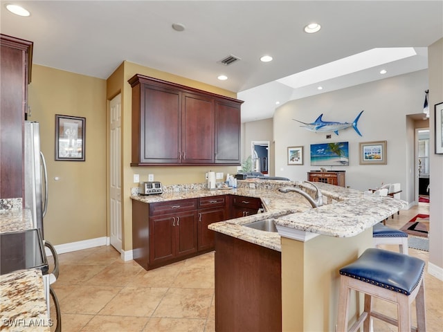 kitchen featuring a kitchen bar, kitchen peninsula, light stone countertops, lofted ceiling with skylight, and sink