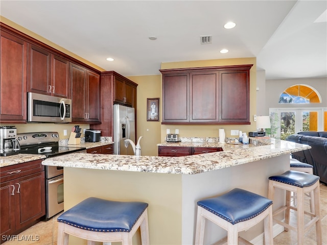 kitchen with light stone countertops, stainless steel appliances, kitchen peninsula, a breakfast bar area, and light tile patterned floors