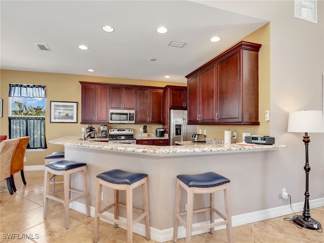 kitchen featuring kitchen peninsula, appliances with stainless steel finishes, a kitchen bar, light stone counters, and light tile patterned floors