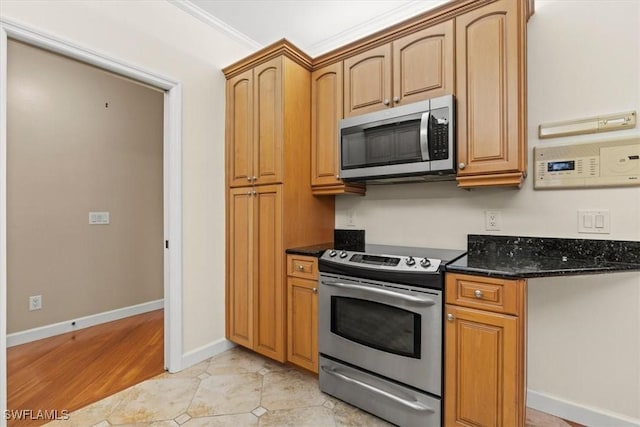 kitchen with dark stone countertops, stainless steel appliances, light tile patterned flooring, crown molding, and baseboards