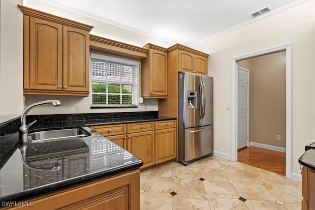 kitchen with sink, crown molding, light tile patterned floors, stainless steel fridge, and dark stone counters