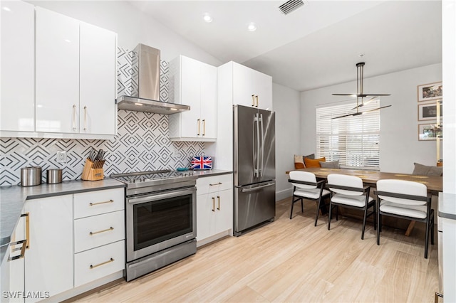 kitchen with stainless steel appliances, white cabinetry, light hardwood / wood-style floors, lofted ceiling, and wall chimney exhaust hood