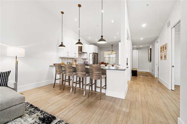 kitchen with light hardwood / wood-style floors, white cabinets, kitchen peninsula, a breakfast bar, and decorative light fixtures