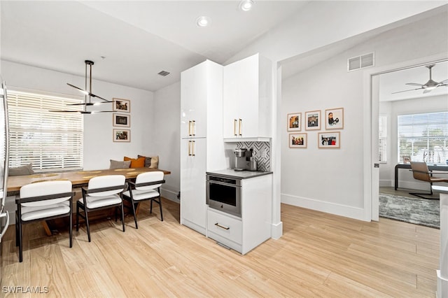 kitchen with white cabinetry, light hardwood / wood-style flooring, lofted ceiling, and stainless steel oven