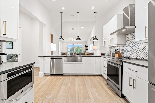 kitchen with white cabinets, stainless steel appliances, decorative light fixtures, and wall chimney range hood