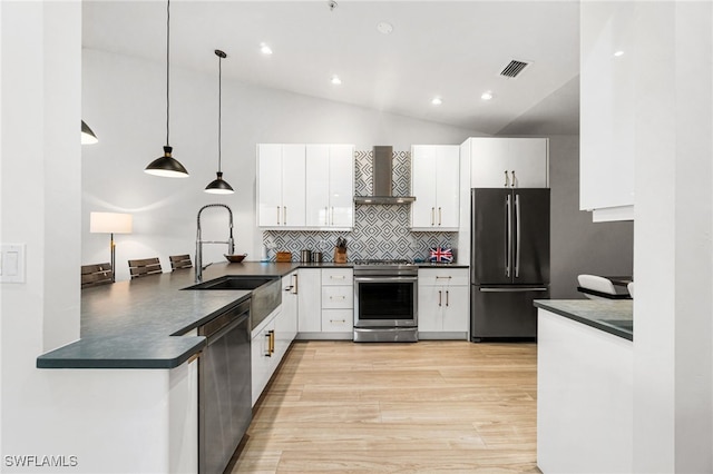 kitchen with pendant lighting, vaulted ceiling, wall chimney exhaust hood, white cabinetry, and appliances with stainless steel finishes