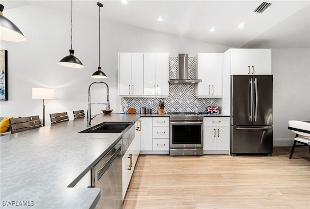 kitchen with stainless steel appliances, white cabinetry, hanging light fixtures, vaulted ceiling, and wall chimney exhaust hood