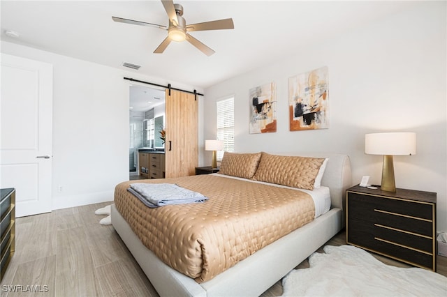 bedroom with a barn door, ceiling fan, and light hardwood / wood-style flooring