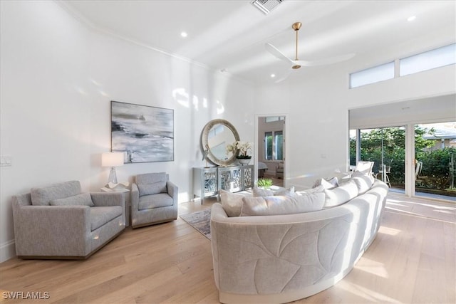 living room featuring ceiling fan, light wood-type flooring, ornamental molding, and a towering ceiling