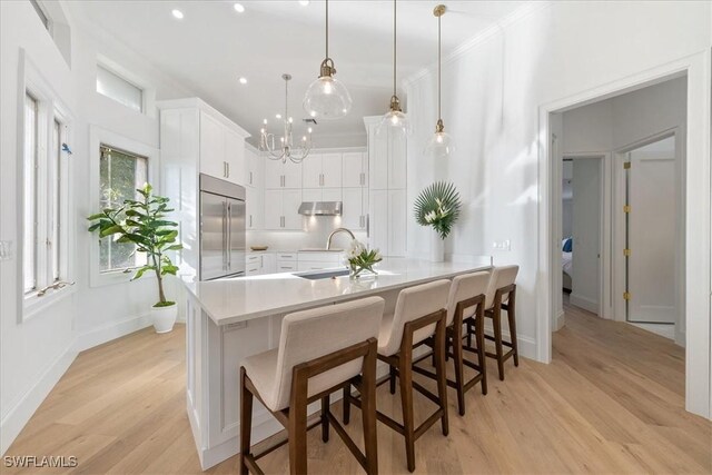 kitchen featuring a kitchen breakfast bar, stainless steel built in refrigerator, white cabinets, light hardwood / wood-style floors, and hanging light fixtures