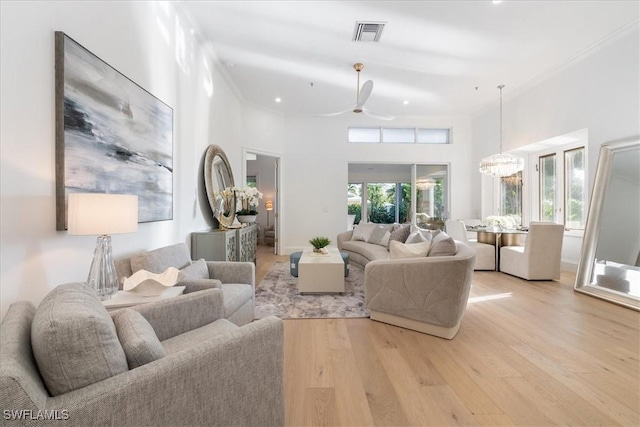 living room with a high ceiling, ceiling fan with notable chandelier, light hardwood / wood-style flooring, and crown molding