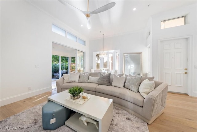 living room with ceiling fan with notable chandelier, light hardwood / wood-style floors, crown molding, and a high ceiling