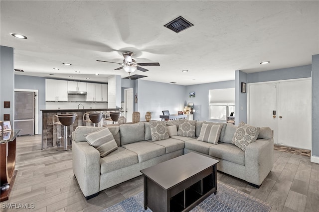 living room with sink, light wood-type flooring, and ceiling fan