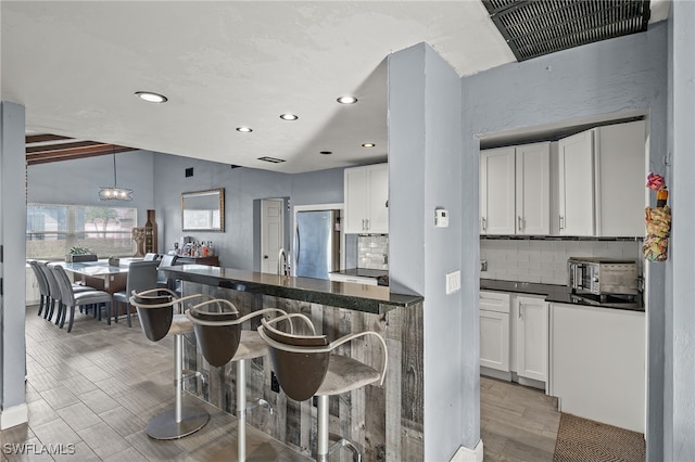 kitchen with light wood-type flooring, hanging light fixtures, white cabinets, stainless steel refrigerator, and a breakfast bar area