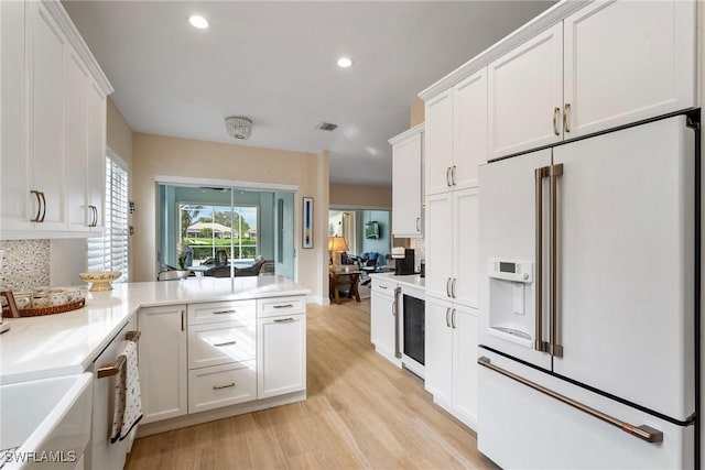 kitchen with high end fridge, wine cooler, white cabinets, decorative backsplash, and light wood-type flooring