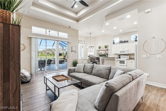 living room featuring a towering ceiling, a tray ceiling, light hardwood / wood-style flooring, and ceiling fan