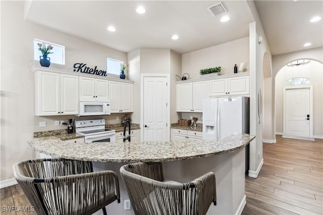 7821 Ashton Rd, Naples, FL 34113 - kitchen with white appliances, a kitchen bar, white cabinets, a peninsula, and light stone counters