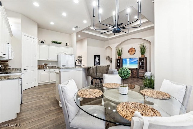 7821 Ashton Rd, Naples, FL 34113 - dining room with arched walkways, wood finished floors, recessed lighting, a chandelier, and a tray ceiling