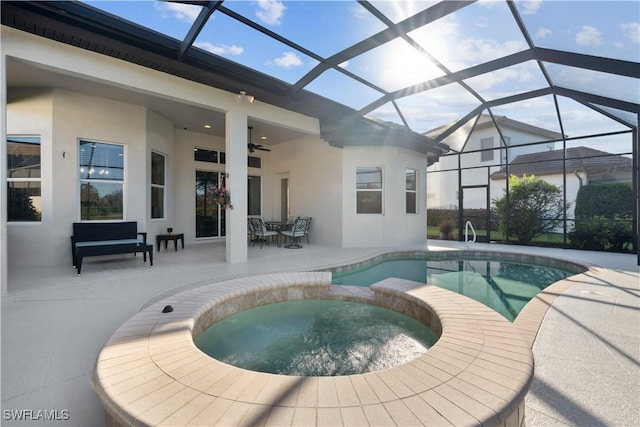 view of swimming pool with glass enclosure, ceiling fan, a patio area, and an in ground hot tub