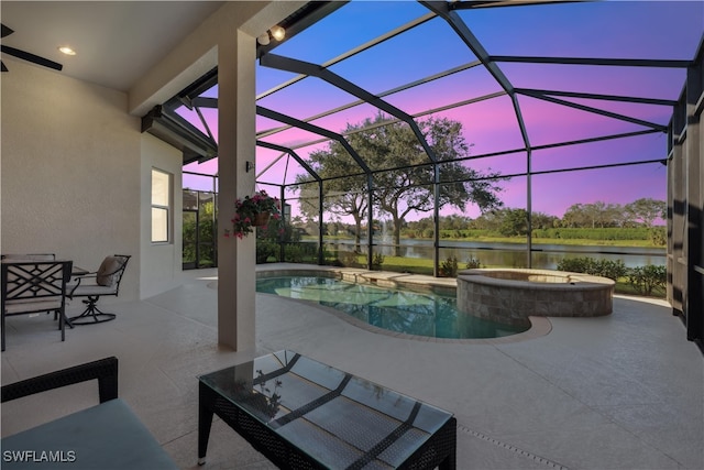 pool at dusk featuring an in ground hot tub, a patio, a water view, and glass enclosure