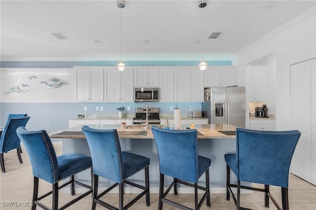 kitchen featuring stainless steel appliances, a kitchen island with sink, white cabinets, and decorative light fixtures