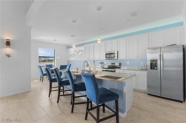 kitchen featuring white cabinetry, appliances with stainless steel finishes, pendant lighting, light stone countertops, and an island with sink