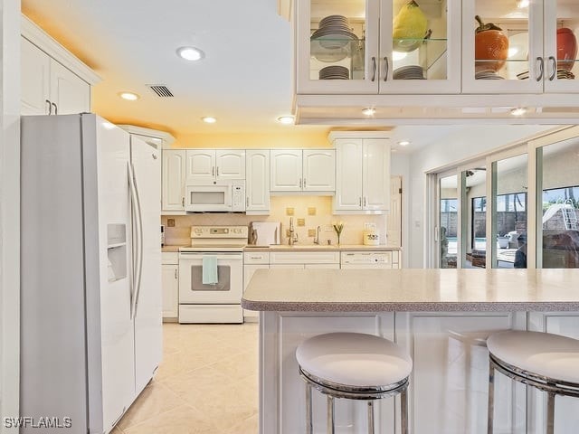 kitchen with white appliances, light tile patterned flooring, white cabinetry, decorative backsplash, and a breakfast bar area