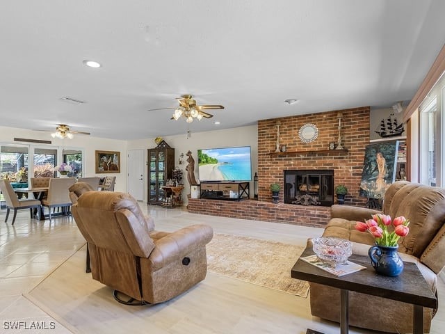 living room with ceiling fan, a brick fireplace, and light tile patterned floors