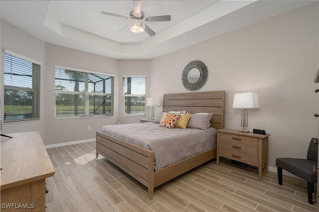 bedroom with ceiling fan, a raised ceiling, baseboards, and wood tiled floor