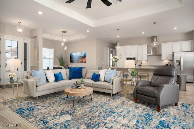 living room featuring ceiling fan, light hardwood / wood-style flooring, and a raised ceiling