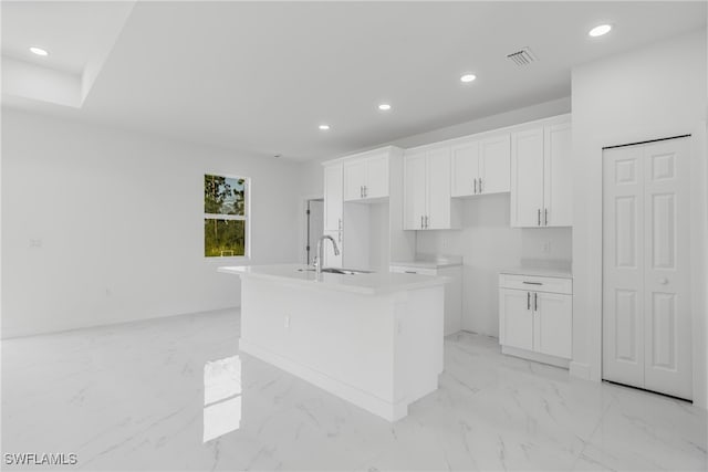 kitchen featuring white cabinetry, sink, and an island with sink