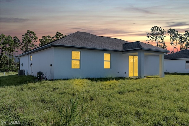 back house at dusk featuring cooling unit and a lawn