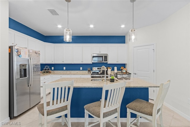 kitchen featuring a center island with sink, light stone counters, white cabinets, appliances with stainless steel finishes, and decorative light fixtures