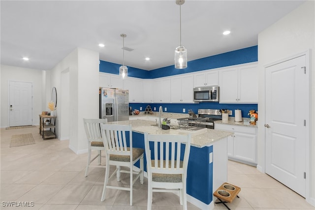 kitchen featuring a center island with sink, white cabinets, hanging light fixtures, light stone countertops, and appliances with stainless steel finishes